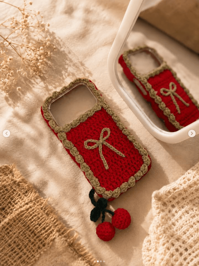 A red crochet phone cover with a bow and a cherry charm